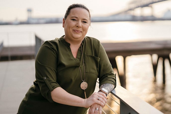 A woman leaning on a rail and posing in front of a body of water.