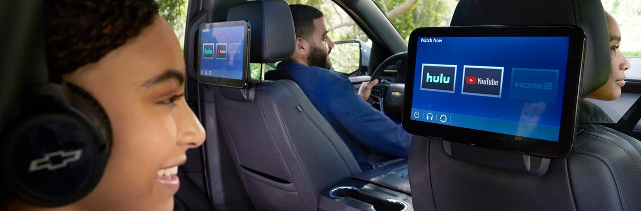 A girl sitting in the passenger seat looking at a tablet device attached to the seat in front of her.