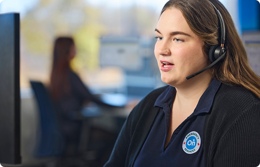 An OnStar advisor wearing a headset speaks while sitting at a computer, with an OnStar logo visible on her uniform.