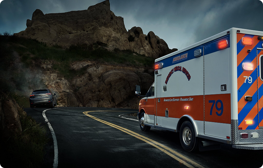 An ambulance with "Advanced Life Support Paramedic Unit" on its side drives on a winding road with a vehicle in the background.