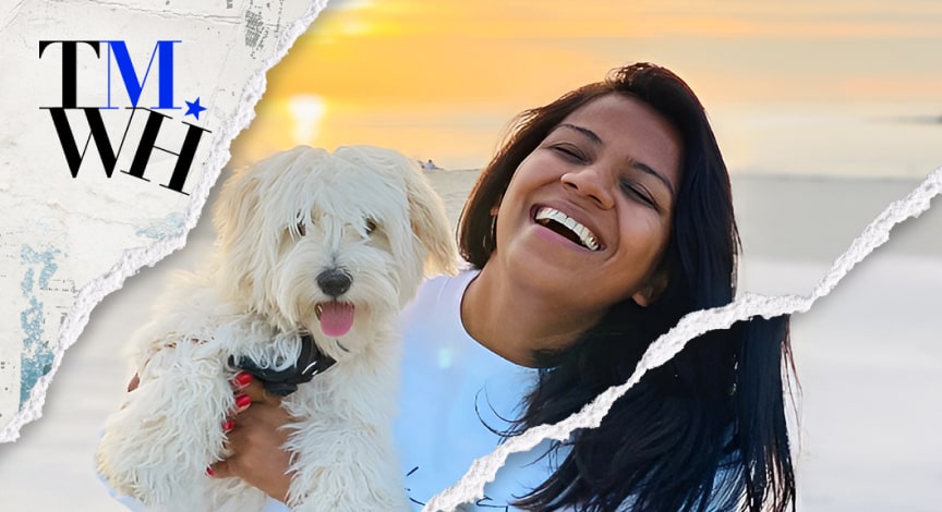 A woman laughing while carrying a dog in front of the beach next to the text overlay of "Tell Me What Happened". 