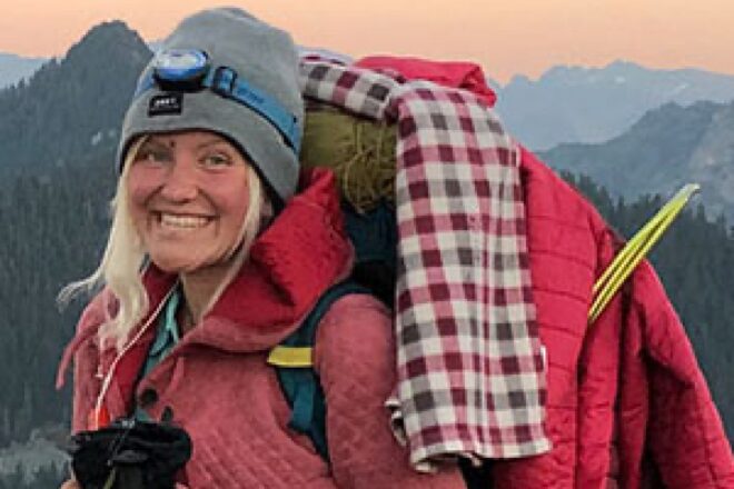 Katharina Grone Carrying Hiking Gear With Mountain View in Background
