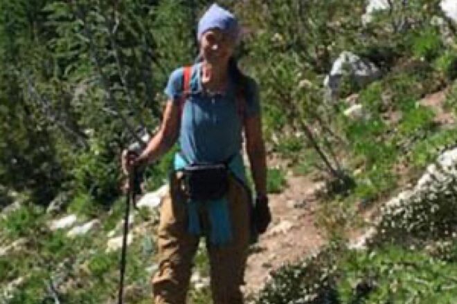 Cheri Higman Wearing Hiking Gear and Helmet with Mountain View in Background
