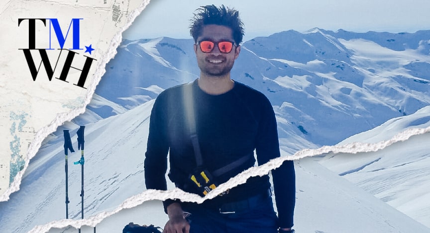 A man wearing sunglasses and traveling gear on top of a snowy mountain next to the text overlay of "Tell Me What Happened". 