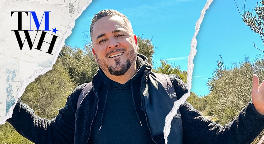 A man posing for a photo outside on a sunny day next to the text overlay of "Tell Me What Happened".