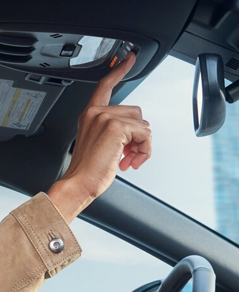 A person's hand presses a button on the overhead console inside a modern vehicle.