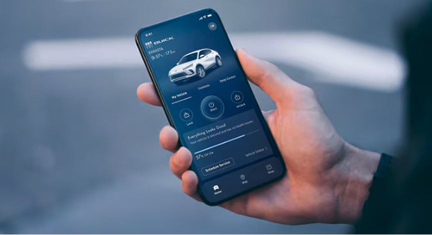 A hand holds a smartphone displaying the myBuick app with a white SUV, showing various vehicle status icons and controls.
