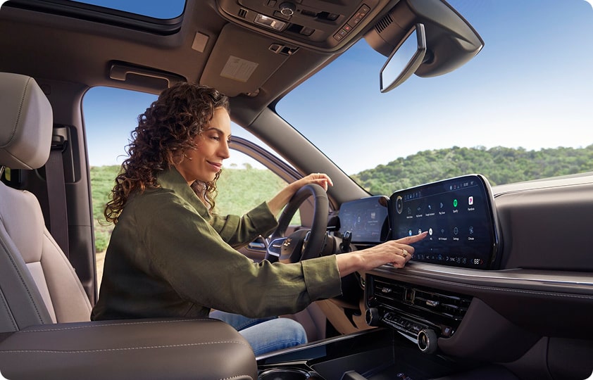 Woman in a car reaching out to touch a large infotainment screen to activate OnStar roadside asistance.