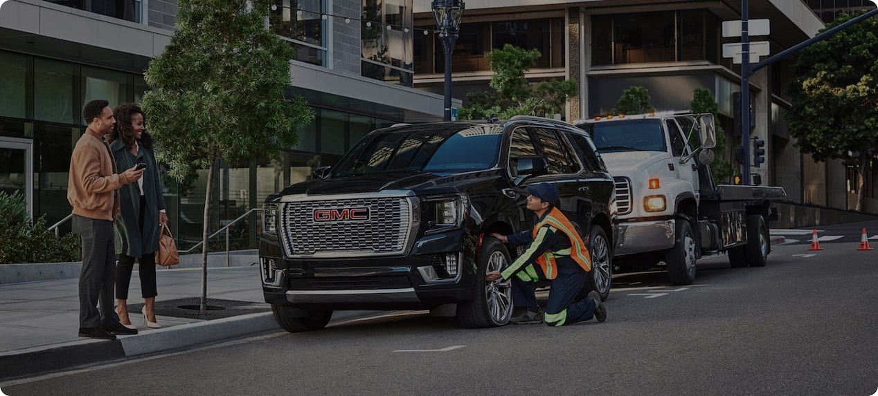 Roadside assistance helping two people with a flat tire on a black GMC SUV.