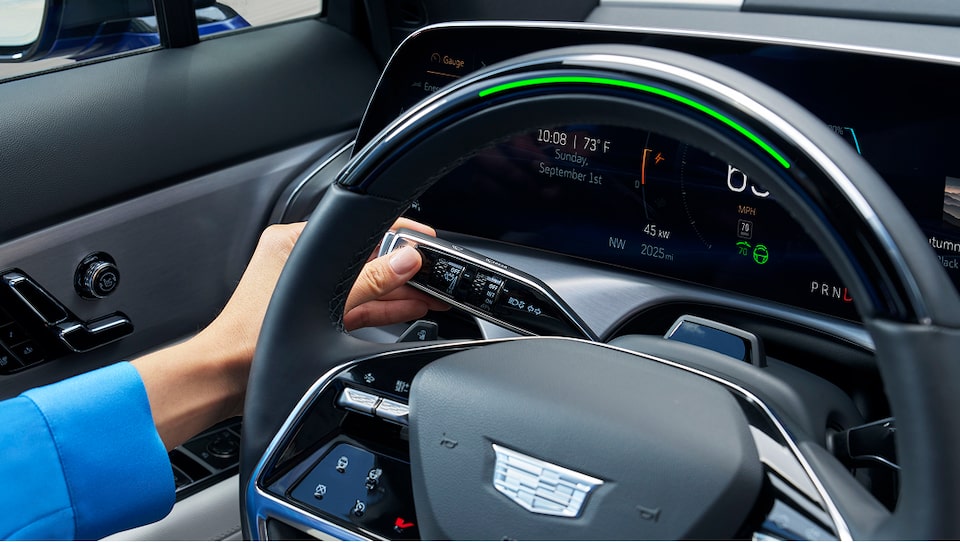 A person's hand activates the turn signal indicator on the Cadillac steering wheel