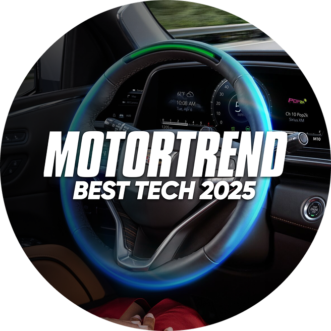 A close-up of a car's steering wheel displays the MOTOR TREND BEST TECH 2025 logo prominently, with a blue and green glowing ring.