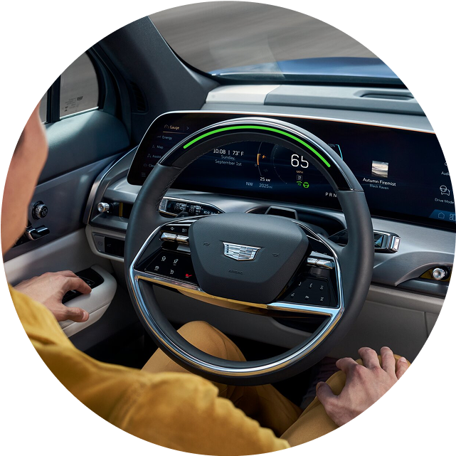 A driver's view inside a Cadillac vehicle, showing the steering wheel with an active green Super Cruise light.