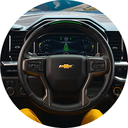 A Chevrolet steering wheel is shown with a green light on its upper rim, and the digital dashboard displays active driver assistance features.