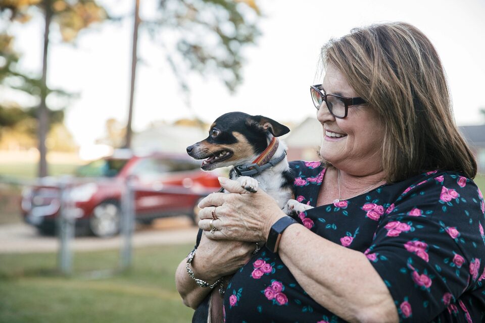 Woman Cuddling a Small Dog and Smiling