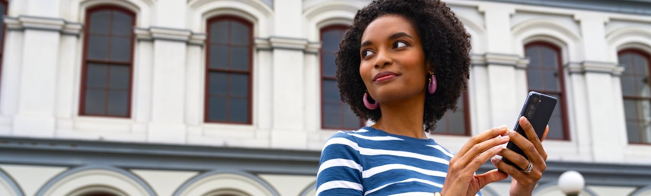 A woman looking to her right and smiling while holding her smartphone.