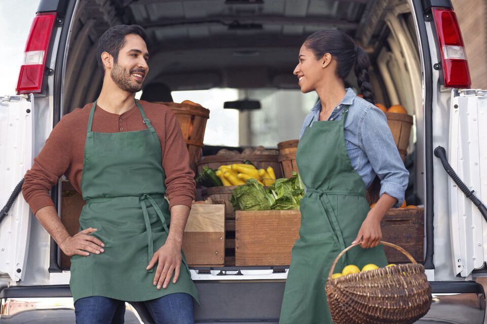 Two People Wearing Aprons Standing at the Rear of a Work Van