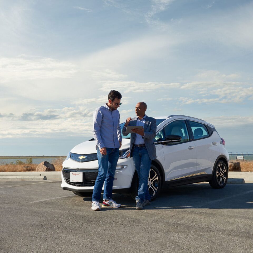 Two Men Looking Over Something Outside Next to a Chevy Car