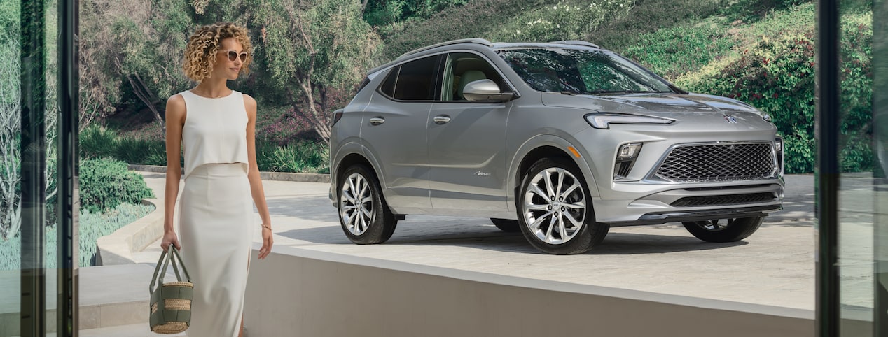 A woman walking into her house with her Buick vehicle parked in the driveway