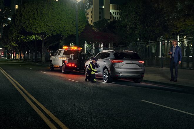 Tow Truck Operator Servicing Flat Tire, on Empty Road at Night Time