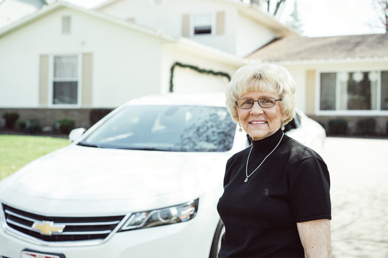 Older Woman Smiling Standing in Front of Chevy Car