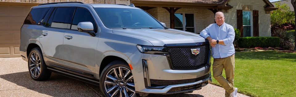 Eric in a blue polo shirt leaning onto the hood of his Cadillac SUV