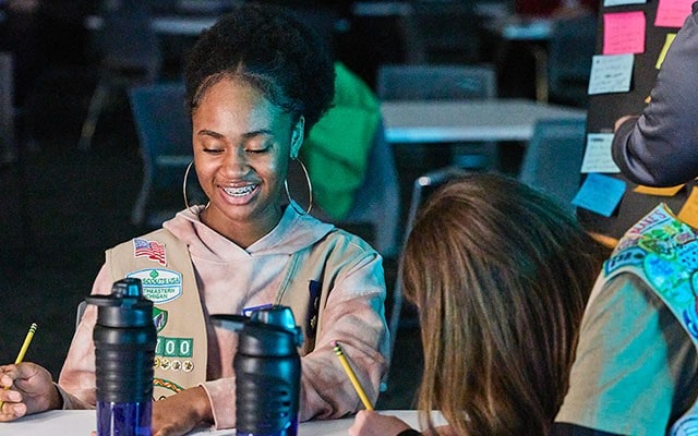 Girl Scouts sitting at a table writing on notepads