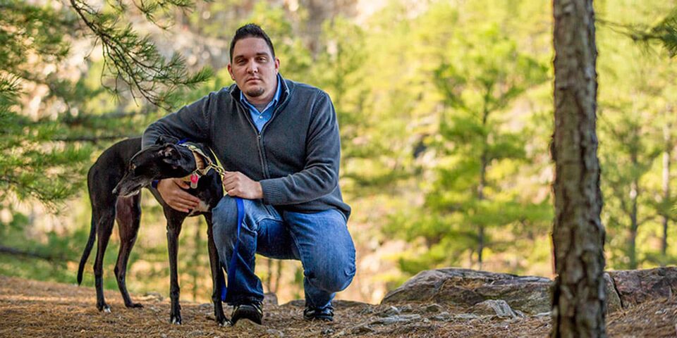 Man Crouching Down to Hug a Dog in a Wooded Area