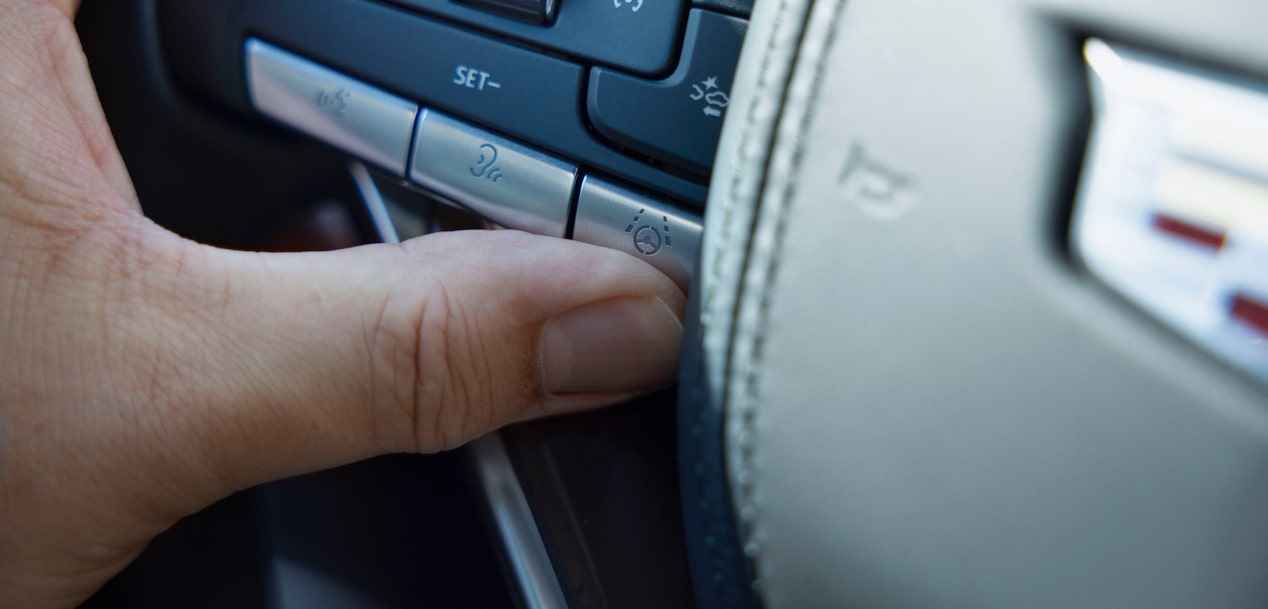 A hand presses a steering wheel button with a super cruise hands-free driving system icon in a cadillac vehicle.