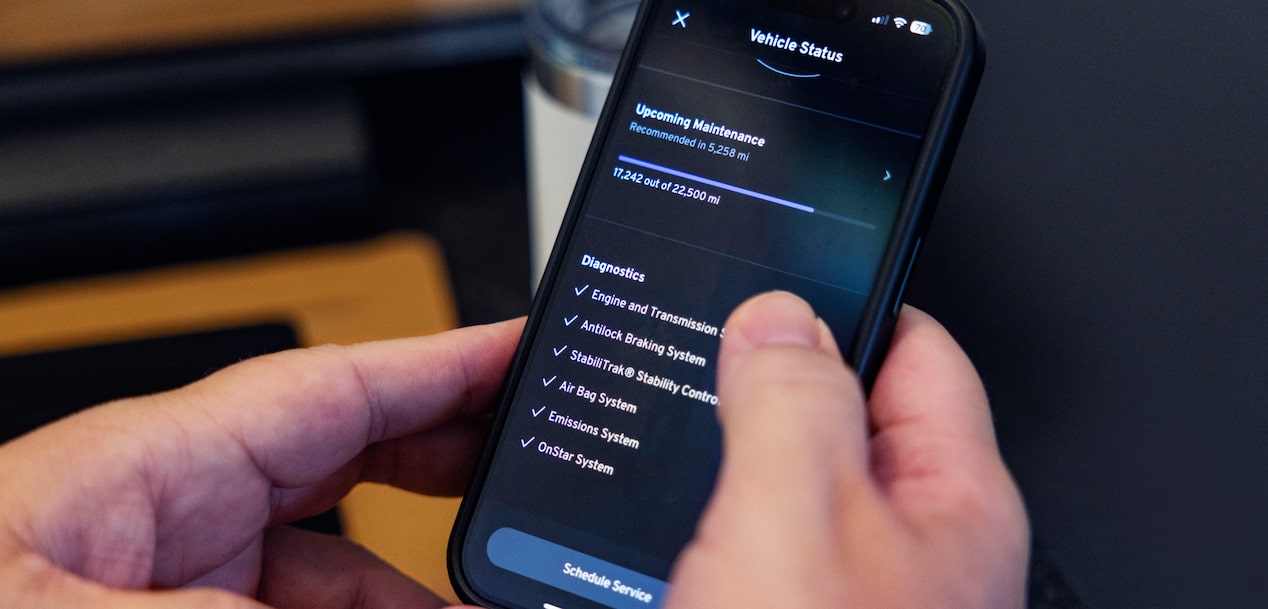 A person's hands hold a smartphone displaying the vehicle status and diagnostics screen of a guardian mobile vehicle app.