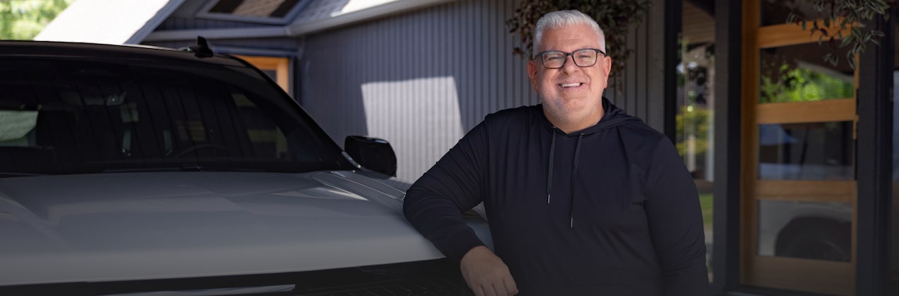  Jason Cupp, a middle-aged man wearing a black hoodie, stands next to the grille of a white Cadillac parked in a garage.