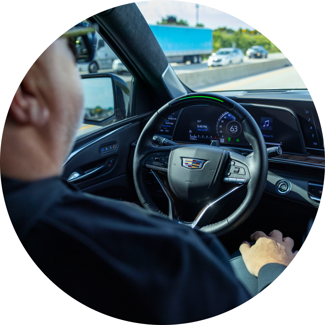 An over-the-shoulder view of Jason Cupp holding the steering wheel of a Cadillac with the Super Cruise hands-free driving system engaged on a highway.