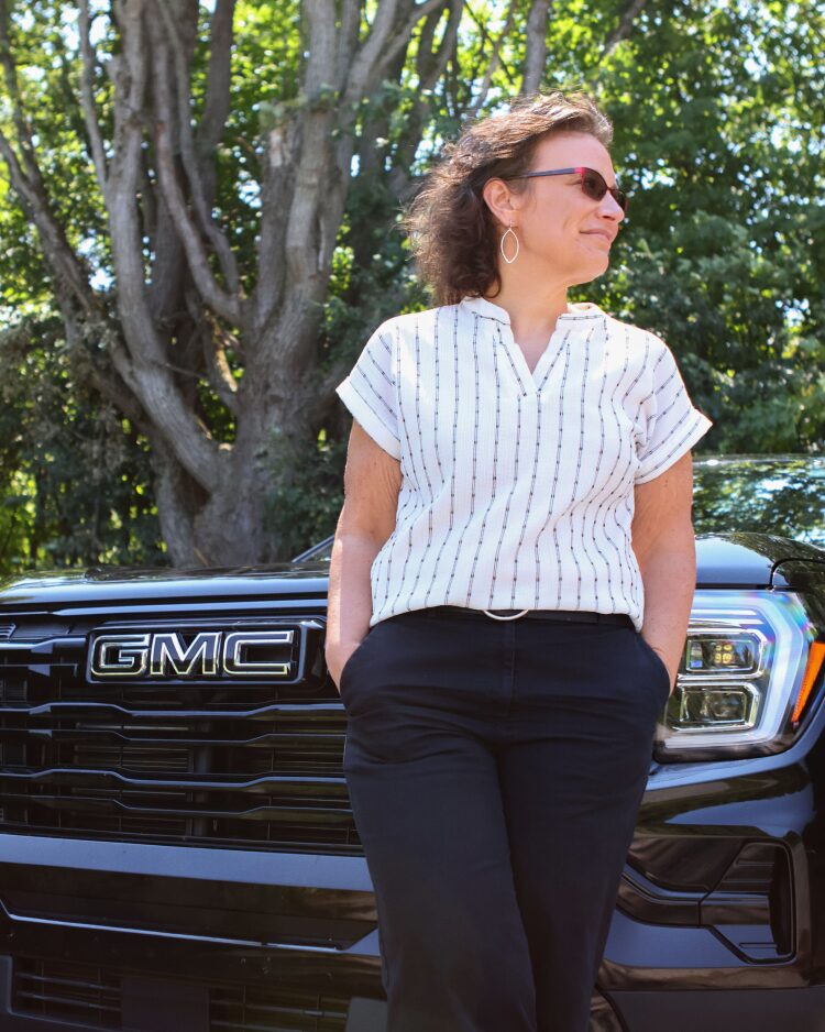 Kristy K stands confidently with hands in her pockets beside a black GMC Terrain, representing a real customer safety story.