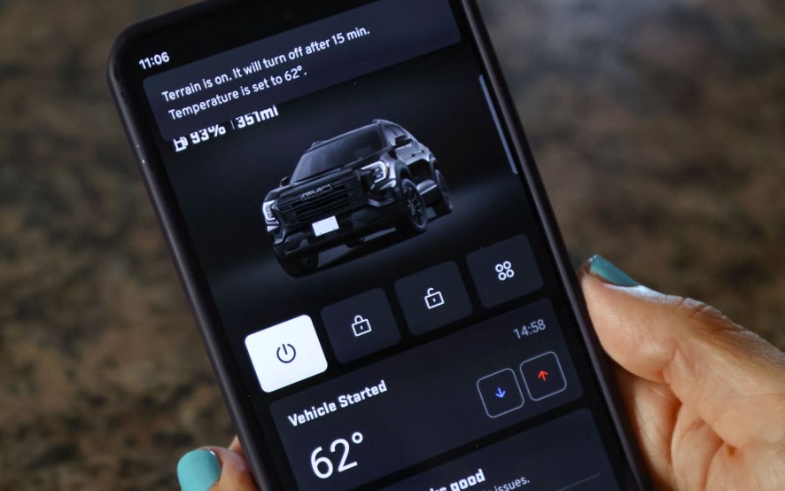 A smartphone displays the MyGMC mobile app, showing a black GMC Terrain and connected vehicle services like remote start and temperature control.
