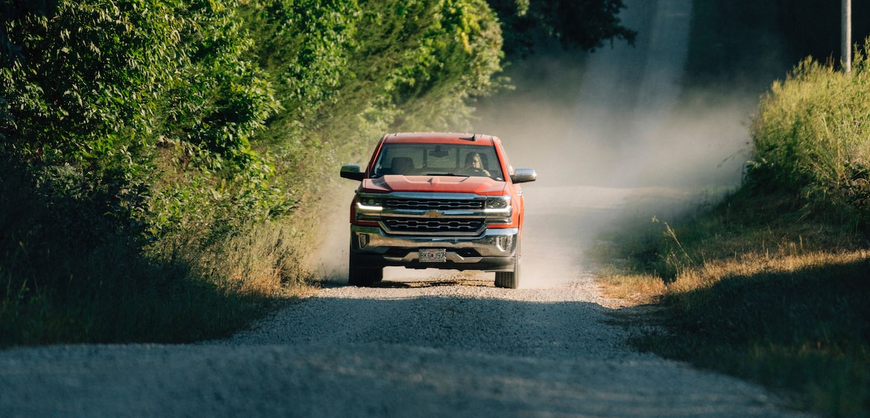 GM Truck Driving Down a Narrow Gravel Road With Dust Kicking Up