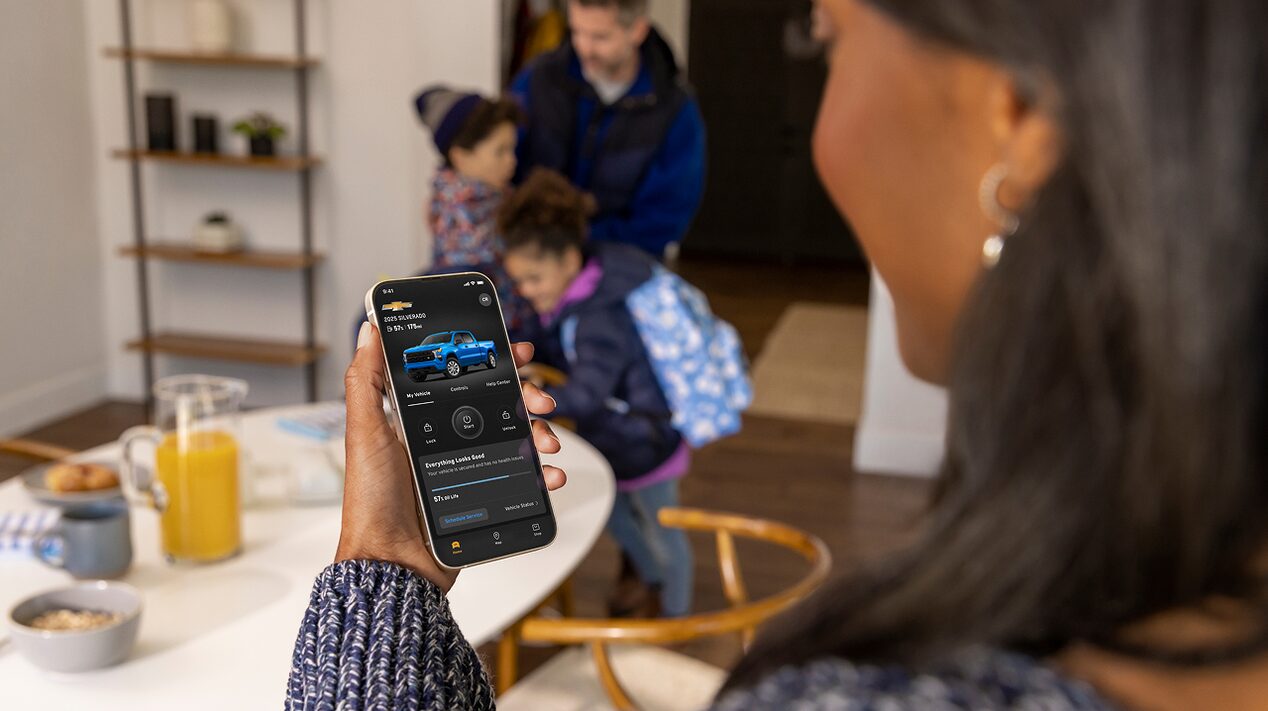 A woman checking her myChevrolet mobile app as her family zips up their coats