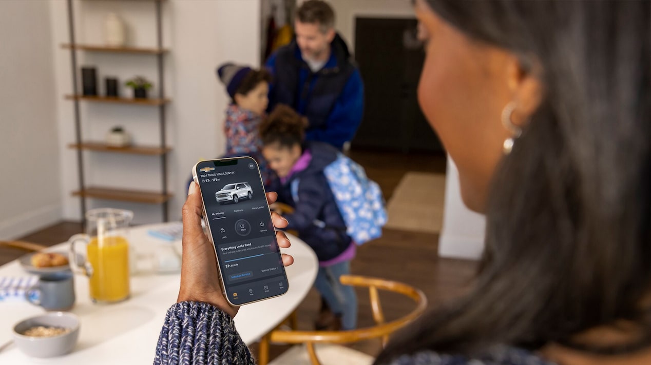 A woman checking her myChevrolet mobile app as her family zips up their coats