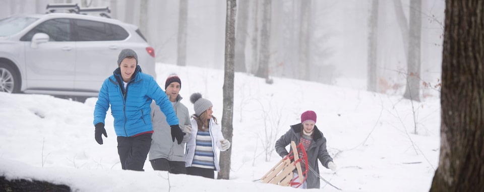 Family going sledding in the snow covered woods with their GM vehicle in the back ground