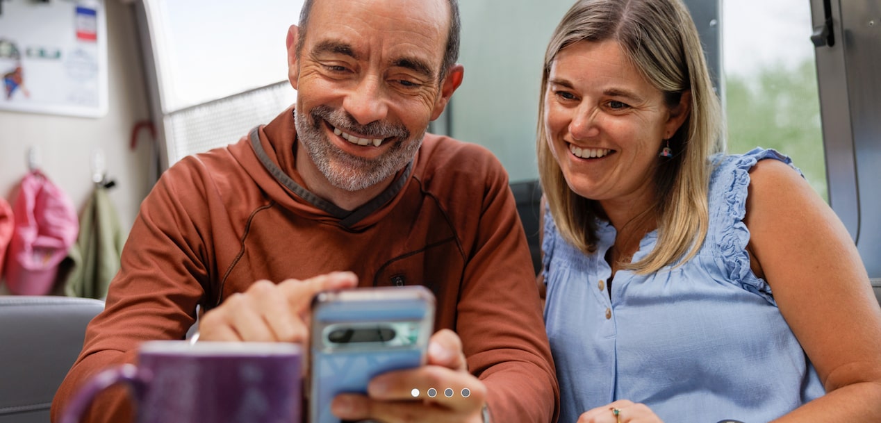 A man and a woman sitting in their camper looking at a smartphone together.