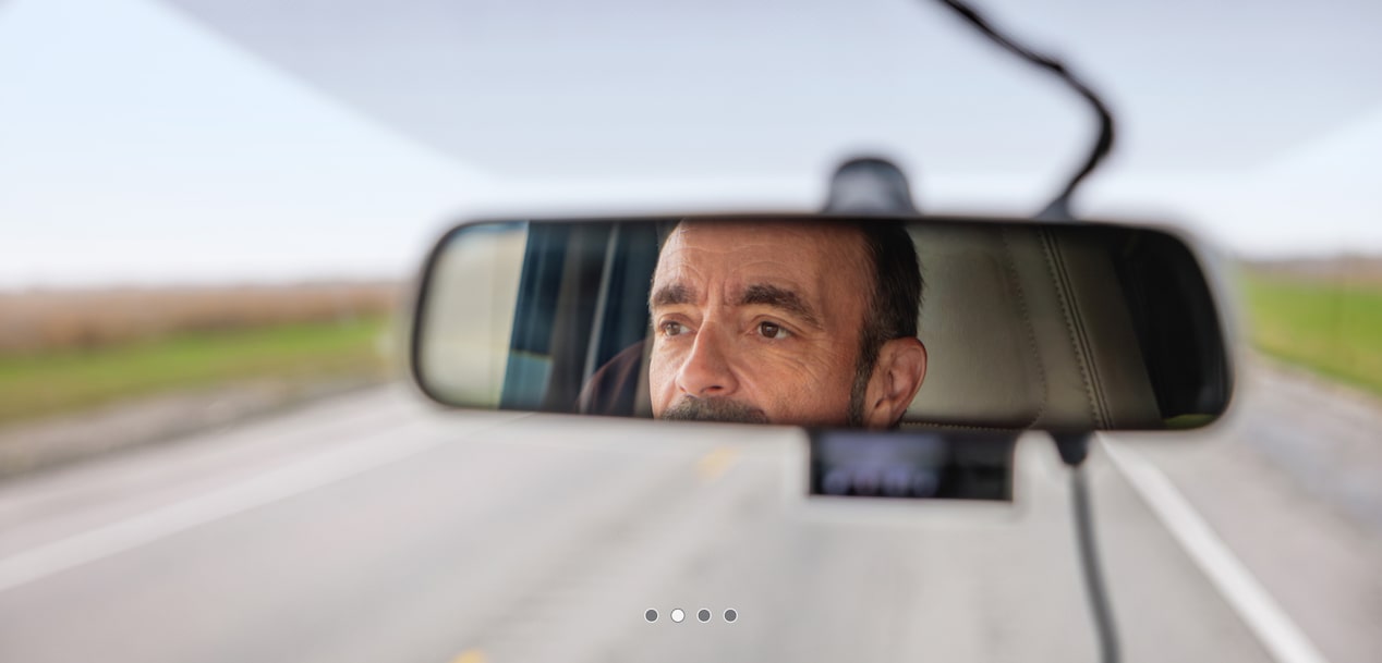 Forward facing view of a man's reflection in the rear view mirror.