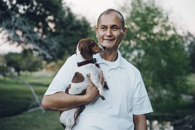 Man Holding a Small Dog and Smiling While Standing Outside
