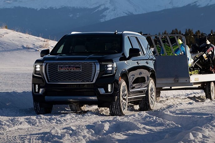 A black GMC SUV tows a trailer across a snowy landscape with mountains in the background.