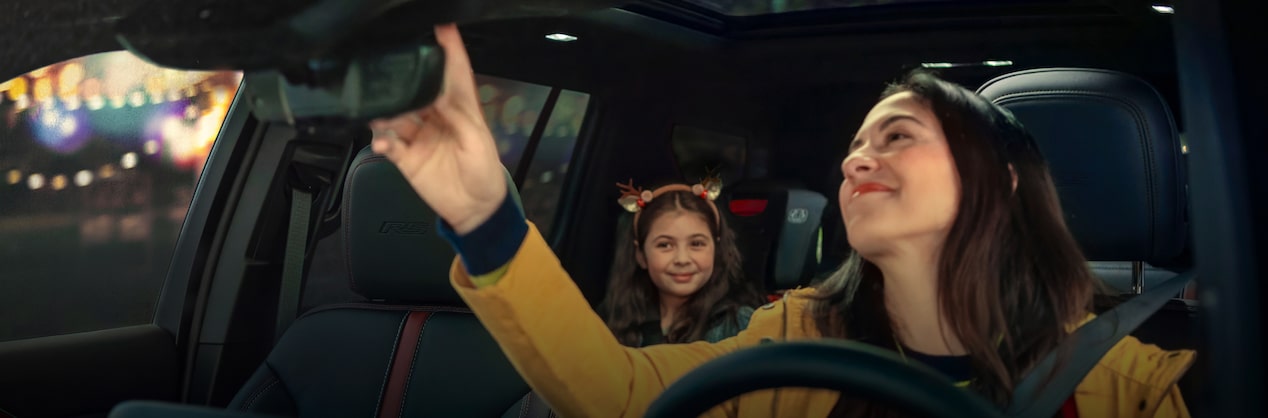 A woman in the driver’s seat pressing the OnStar button while smiling at her daughter in the back seat.