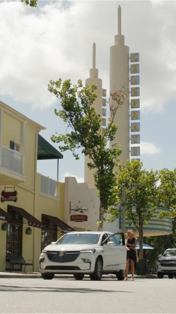 Far three quarters view of a white vehicle on the road next to a yellow building