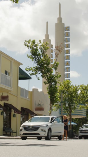 Far three quarters view of a white vehicle on the road next to a yellow building