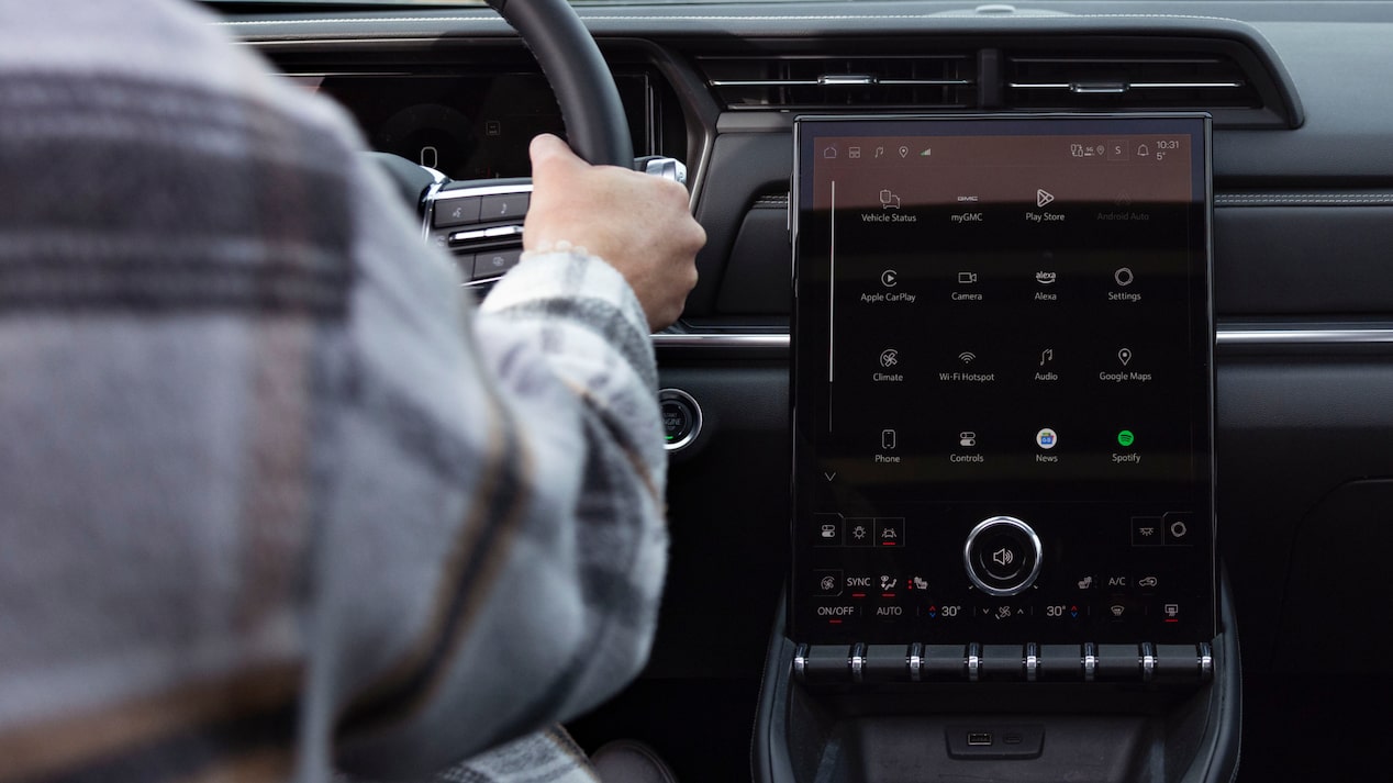 A driver's hand is on the steering wheel next to a large vertical infotainment screen inside a GMC Terrain.