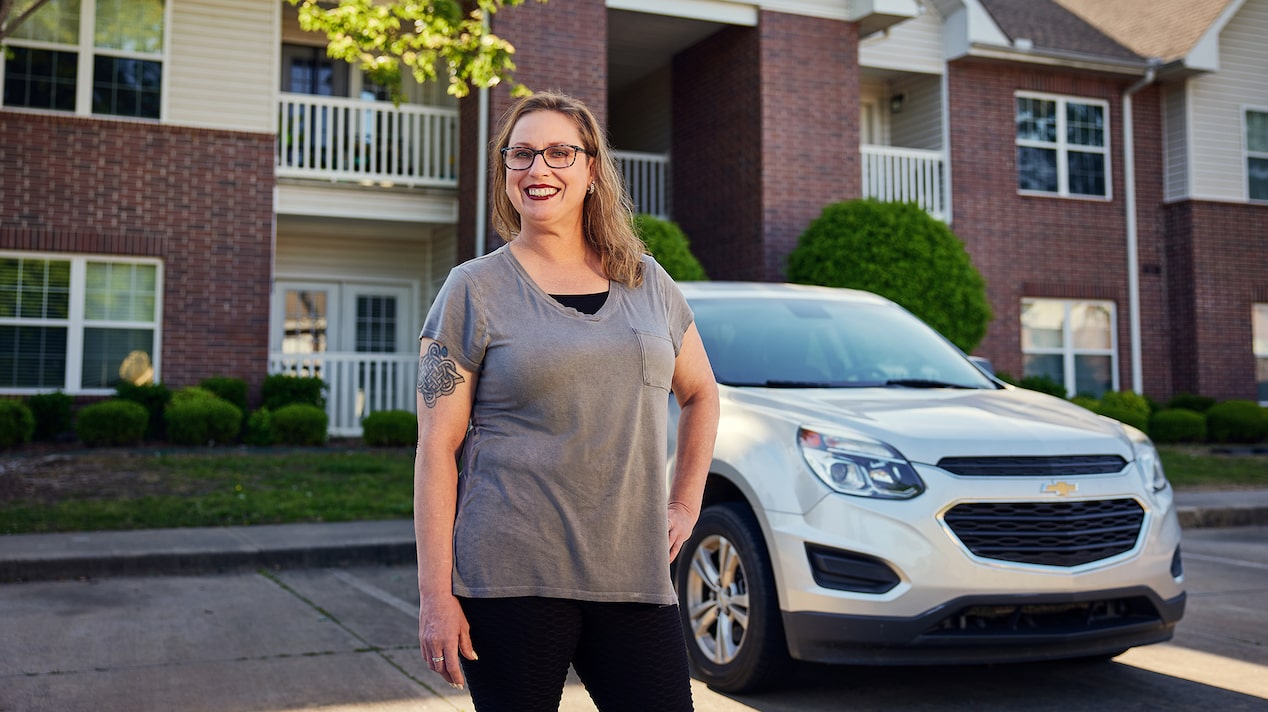 Nicole Kutas smiles while standing next to her Chevy in front of an apartment building.