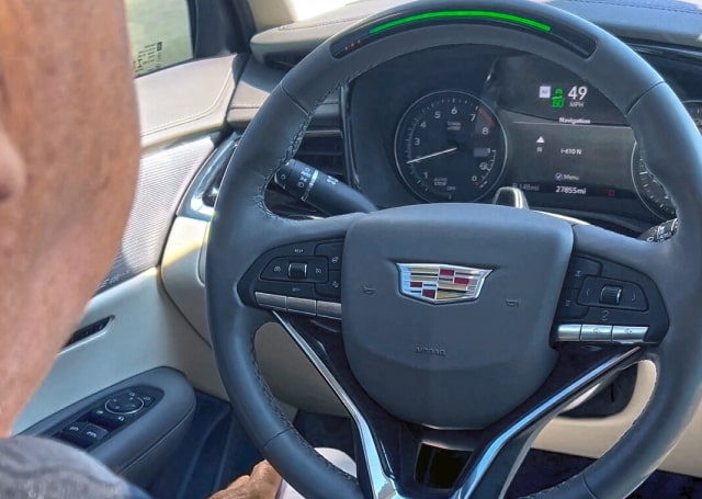 A man in the driver's seat with a close up of the Cadillac steering wheel