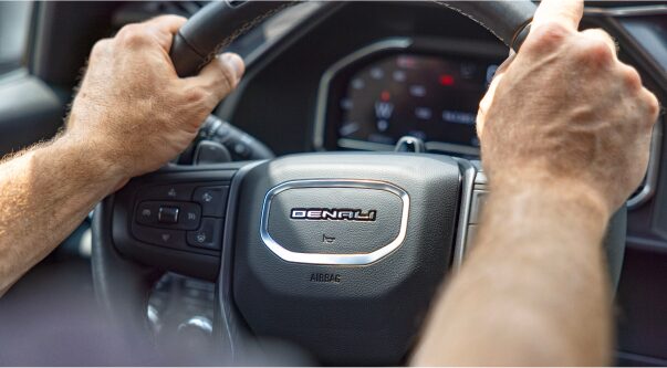 A person's hands holding the steering wheel of a GMC vehicle