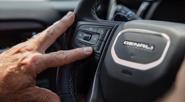 A close-up of a driver pressing the Super Cruise button on the steering wheel