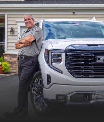 Marco C. leaning on his white GMC Sierra truck that is parked in his driveway